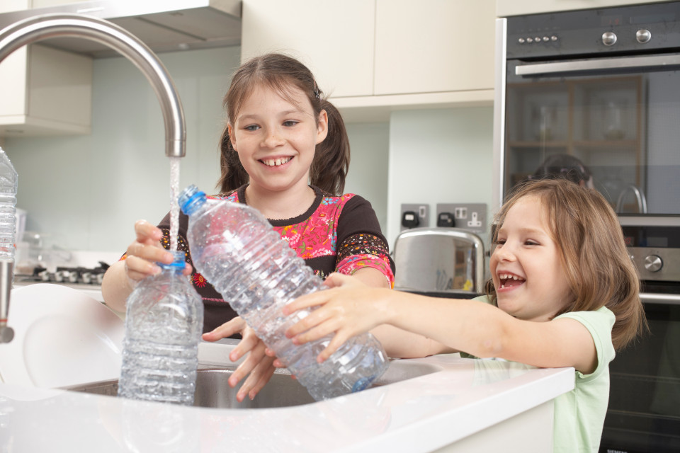 Girls filling up water bottle in kitchen